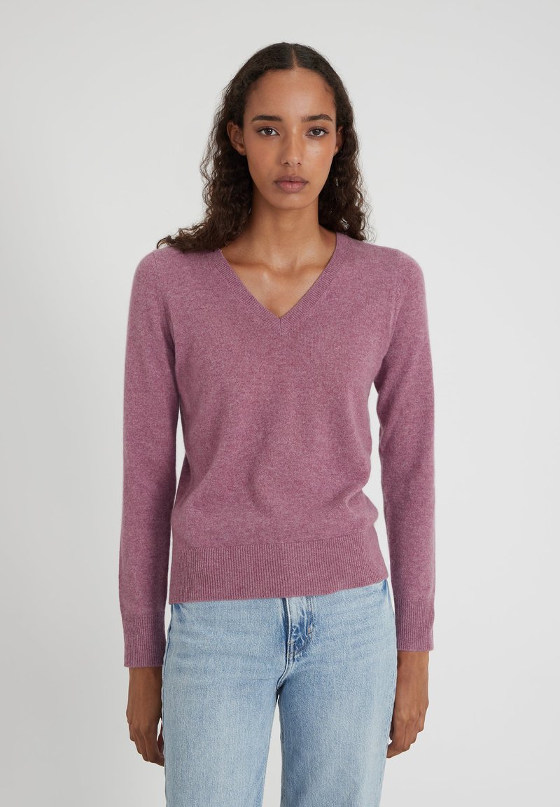 Helllila V-Ausschnitt Pullover aus weichem Material mit langen Ärmeln und geripptem Saum. Kombiniert mit hellblauen, geraden Jeans.