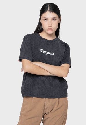 Camiseta negra de algodón con el logo "Dreamers Kaotiko Society" en blanco, de manga corta, corte relajado y con un acabado ligeramente texturizado.