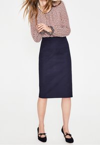 Blusa a maniche lunghe, a fantasia, di colore rosa chiaro e nero, abbinata a una gonna a tubo blu navy, lunga fino al ginocchio. Ballerine nere con fiocchi.