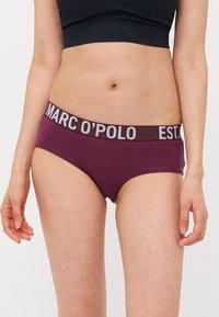 Ljubičaste pamukaste kratke gaćice s elastičnom trakom koja sadrži sive natpise "MARC O'POLO" i "EST.". Glatka tekstura i prilagođen dizajn.