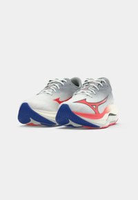 Scarpe sportive grigio chiaro con lacci bianchi, dettagli rossi e suola blu. Presentano una tomaia testurizzata e un tallone curvato per il supporto.