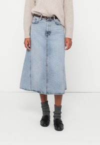 Person iført lys blå denim midi-nederdel, beige sweater stukket ind, sort bælte, grå slouchy sokker og sorte loafers, som står imod en hvid baggrund.