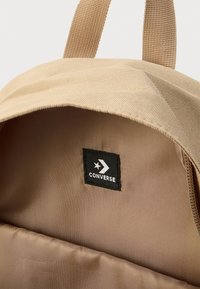 Εσωτερικό μπεζ σακιδίου πλάτης που δείχνει απαλό ύφασμα με μαύρη ετικέτα λογότυπου "Converse". Διαθέτει μαλακή υφή και απλό σχεδιασμό χωρίς επιπλέον σχέδια.