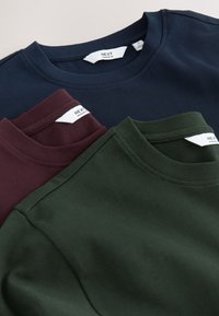 Tres camisetas de cuello redondo en azul marino, burdeos y verde oscuro, hechas de tela suave con cuellos acanalados y etiquetas visibles en el interior.