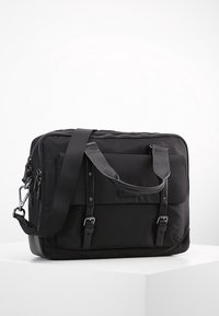 Svart tyg messenger-väska med dubbla handtag och en avtagbar axelrem. Har en framficka med spännen och ett zip-up huvudfack.