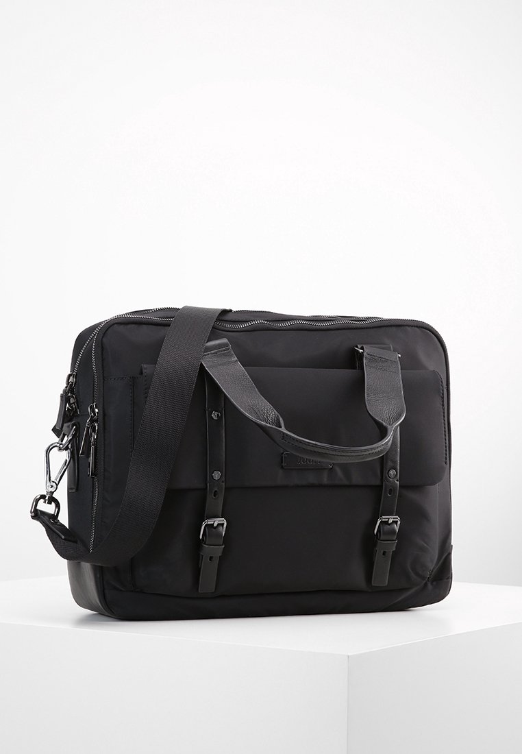 Svart tyg messenger-väska med dubbla handtag och en avtagbar axelrem. Har en framficka med spännen och ett zip-up huvudfack.