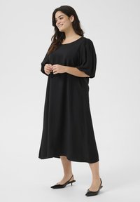 Abito midi nero in tessuto morbido con maniche a sbuffo corte, scollatura rotonda e silhouette fluida, abbinato a scarpe flat slingback nere.