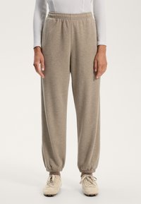 Vaaleanruskeat collegehousut pehmeästä materiaalista, joissa on joustava vyötärö ja kuminauha lahkeissa, yhdistettynä vaaleankermanvärisiin lenkkareihin.