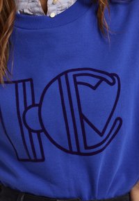Royalblaues Sweatshirt mit einem großen, dunkelblauen grafischen Design mit Linien und Kurven. Gerippter Ausschnitt und weicher Stoff.