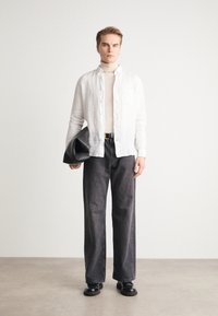 Weißes Leinen-Hemd mit Knöpfen, beiger Rollkragenpullover, dunkelgraue weite Jeans, schwarzer Gürtel, schwarze übergroße Clutch, schwarze Schuhe, minimalistisches Design.