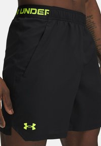 Schwarze Sportshorts mit einem dehnbaren Bund, der mit einem leuchtend grünen "Under Armour"-Logo und Seitentaschen ausgestattet ist. Aus leichtem Material gefertigt.