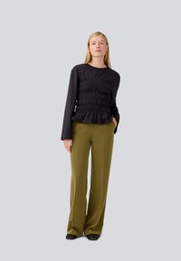 Black long-sleeve top with gathered texture at the front, paired with high-waisted olive green wide-leg trousers, and black shoes.