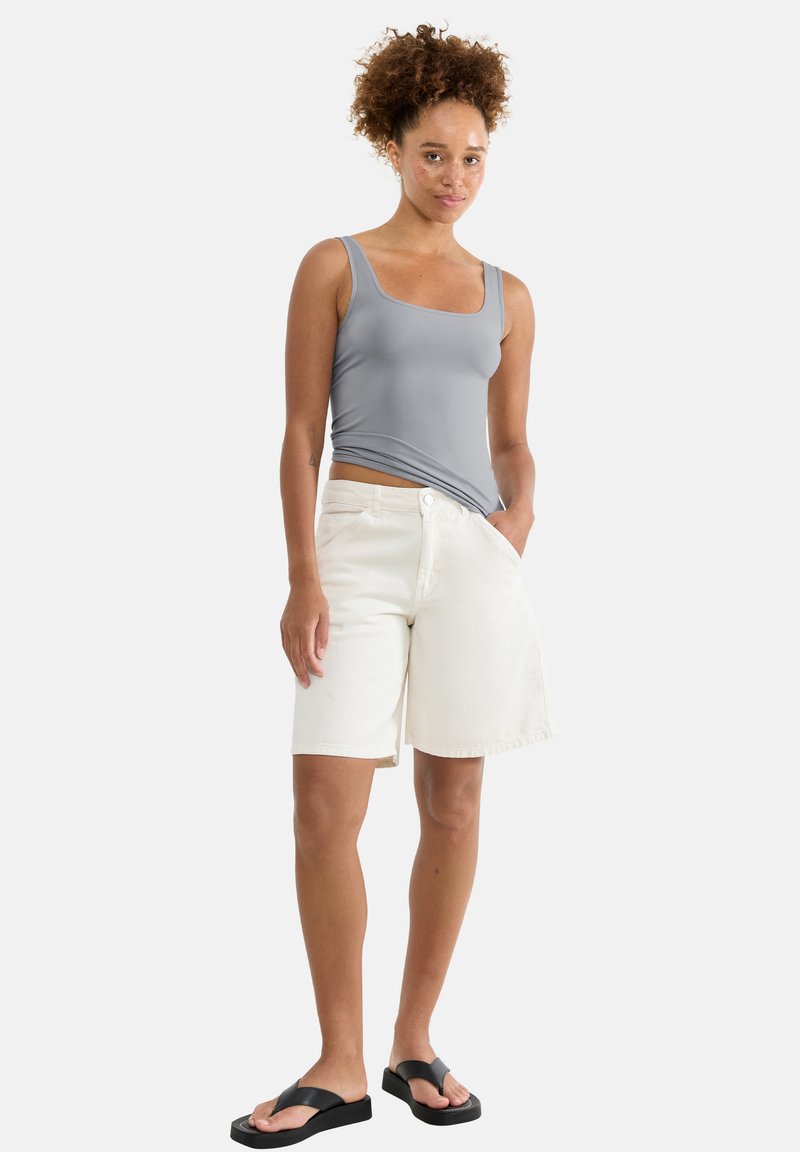 Haut gris sans manches, short en denim blanc et tongs noires. Le short présente une taille haute et des poches latérales, avec une texture lisse.
