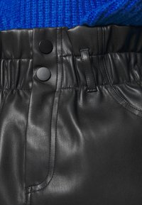 Pas černých kožených kalhot s dvěma černými patentkami a poutky na opasek, doplněný modrým texturovaným pleteným svetrem zasunutým dovnitř.