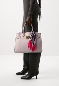 Borsa in pelle rosa chiaro con manici arrotondati, una chiusura dorata e un foulard multicolore legato a un manico. Forma rettangolare slim.