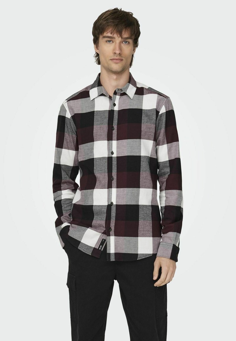 Camisa de cuadros de manga larga en negro, blanco y burdeos. Presenta un cierre frontal de botones, cuello y patrones de cuadros en contraste.