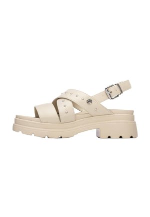 Sandalias de cuero beige con suela gruesa, tiras cruzadas y tachuelas decorativas. Tira ajustable en el tobillo con hebilla de metal.