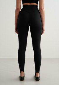 Höga svarta leggings med en mjuk textur, åtsittande design och sömdetaljer på baksidan, tillsammans med svarta skor.