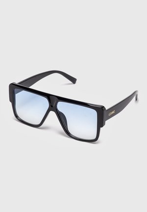 Gafas de sol cuadradas de gran tamaño en color negro con lentes de degradado azul y la palabra "GIANNI" en dorado en la patilla, exhibidas sobre un fondo claro y sencillo.