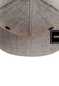 Grå caps med en strukturert stoff, lett buet skygge og en svart etikett med "MSTR"-logo på siden.