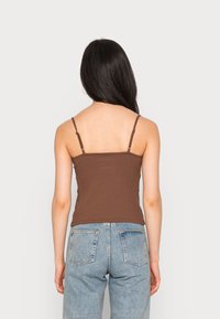 Top de tanque castanho com textura em relevo, alças ajustáveis finas, design justo e bainha reta, combinado com jeans de ganga azul claro de cintura alta.