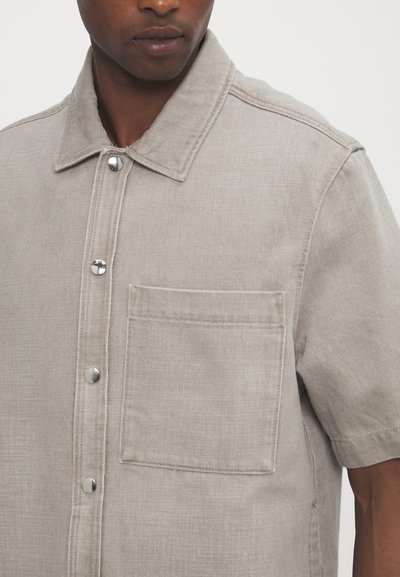 Lichtbeige kortom shirt gemaakt van gestructureerde stof, met een puntkraag, metalen drukknoopjes en een borstzak.