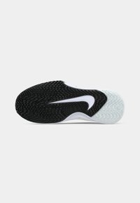 Semelle d’une chaussure de sport avec une semelle texturée noire et blanche et un logo swoosh blanc au centre sur un fond clair uni.
