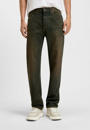 Green denim jeans with a straight-leg fit, featuring five pockets, a button closure, and contrasting stitching details. Worn with light sneakers.