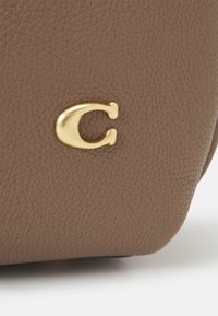 Surface en cuir brun texturé avec un petit emblème en métal doré en forme de lettre C attaché.