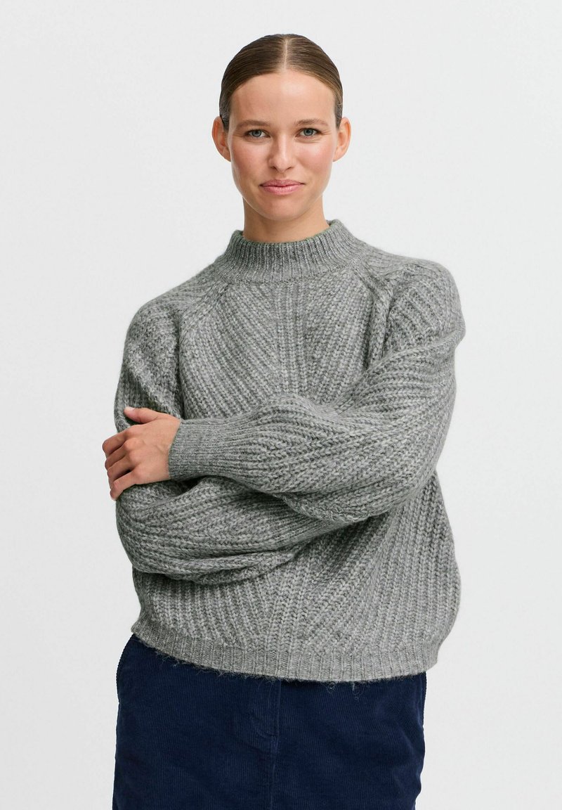 Gray knit sweater with a high neck, featuring ribbed texture and oversized fit, paired with a dark blue bottom.