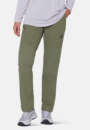 Person iført olivengrønne udendørsbukser med lynlåslomme i siden, kombineret med lyse lilla sneakers og en lysegrå langærmet top.