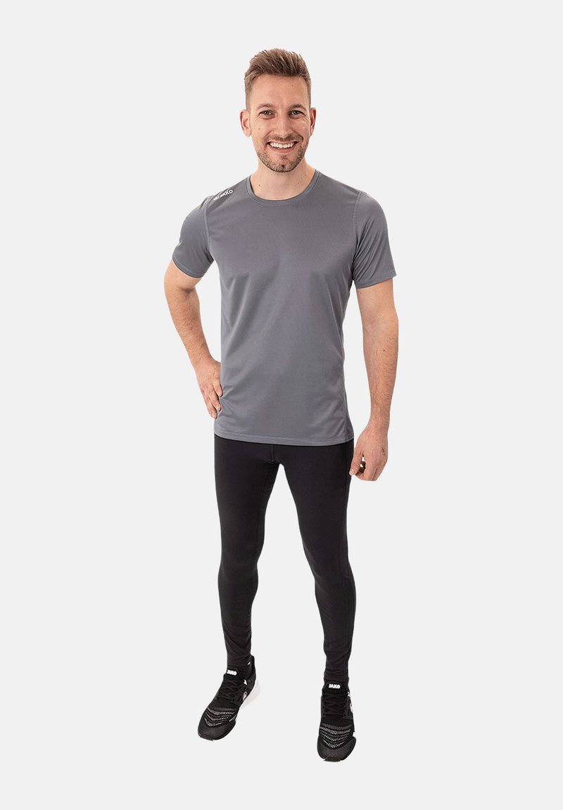 Graues Sport-T-Shirt mit kurzen Ärmeln, tailliertem Design, kombiniert mit schwarzen Leggings und schwarzen Sport Schuhen. Schlichte und funktionale Optik.