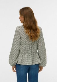 Ruuduline pluus peplum tüüpi vöökoha, pikkade balloon-sleeved varrukate ja kogumise detailidega taga. Kangas on pehme ja tekstuuriga.