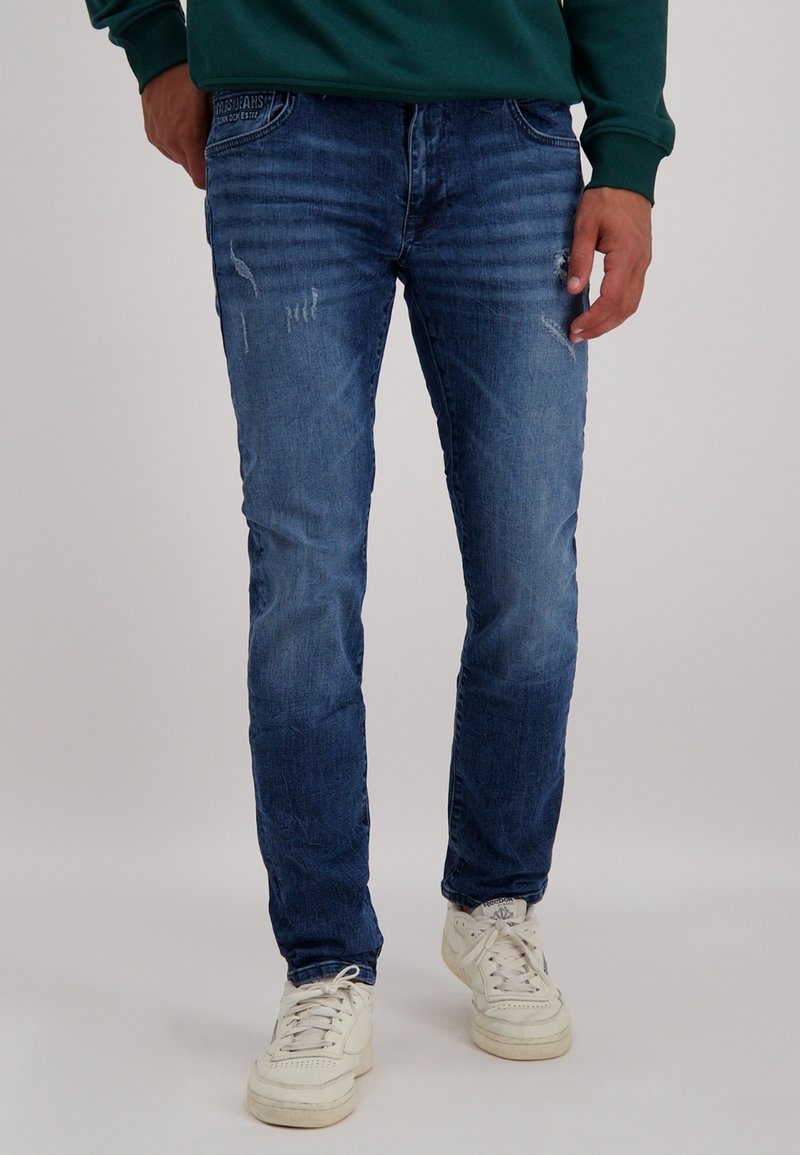 Slim-fit blauwe denim jeans met lichte slijtage, vervaagde textuur en contrasterende stiksels. Gemaakt met witte sneakers.