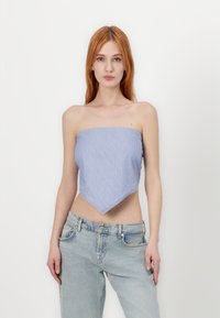 Modrý a bílý pruhovaný top z látky s bandeau designem a špičatým lemem. Stylizovaný s světle modrými džíny s vysokým pasem.