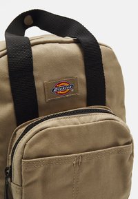 Beezik kangast seljakott mustade nätimise rihmadega, millel on lukuga esikott ja logo plaastriga. Tekstureeritud pind ja vastupidav kujundus.