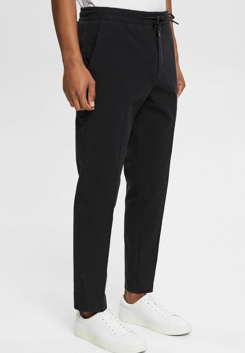 Czarne zwężane spodnie z elastycznym paskiem i sznurkiem do regulacji. Wykonane z gładkiej tkaniny, z bocznymi kieszeniami i prostym, schludnym krojem.