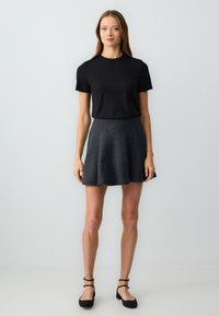 Schwarz kurzärmliges Rippoberteil zusammen mit einem ausgestellten dunkelgrauen Rock. Der Rock hat eine glatte Textur und reicht bis oberhalb des Knies. Schwarze Ballerinas mit Knöchelriemen.