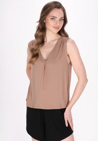 Top senza maniche color sabbia con scollatura a V e dettaglio plissettato, abbinato a pantaloni corti neri. Il tessuto sembra morbido e leggero, offrendo una vestibilità comoda.