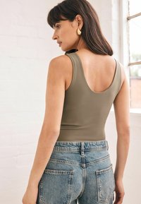 Un top verde măsliniu cu un decolteu rotund, purtat cu blugi din denim ușor albastri, cu talie înaltă, ce prezintă un design clasic cu cinci buzunare.
