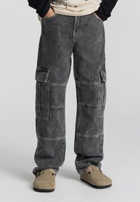Pantaloni cargo in denim grigio scuro con molteplici tasche e una vestibilità comoda. Il materiale ha una texture morbida e un aspetto leggermente sbiadito.