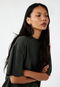 Camiseta de gran tamaño de color gris oscuro con mangas cortas, hecha de una tela texturizada. Presenta un cuello redondo y un corte relajado.