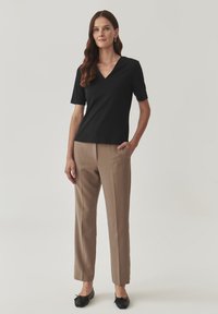 Haut noir à manches courtes avec un décolleté en V, associé à un pantalon beige ajusté et des ballerines noires avec un détail en nœud. Tissu lisse et design ajusté.