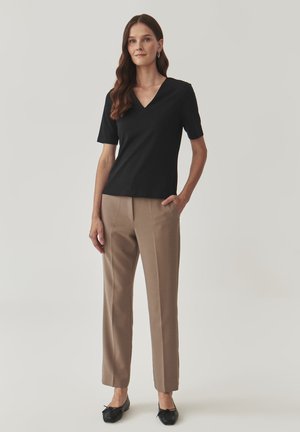 Haut noir à manches courtes avec un décolleté en V, associé à un pantalon beige ajusté et des ballerines noires avec un détail en nœud. Tissu lisse et design ajusté.