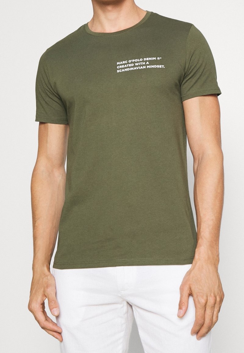 Camiseta de algodón verde oliva con cuello redondo y mangas cortas; presenta texto en blanco que dice "MARC O'POLO DENIM" en la parte delantera.