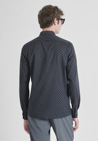Camicia a maniche lunghe con motivo scuro caratterizzata da una stampa geometrica in tonalità blu contrastanti. Tessuto liscio con una consistenza morbida.