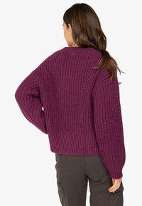 Strickpullover in tiefpurpur. Verfügt über ein strukturiertes Muster, einen oversized Schnitt und gerippte Säume. Etikett sichtbar am hinteren Kragen.