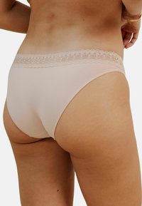 Culotte de bikini en coton beige avec une finition en dentelle autour de la taille, offrant une texture lisse et un design à couverture minimale.