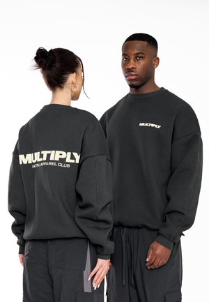 Donkergrijze sweaters met een ontspannen ontwerp en verlaagde schouders. Op de achterkant staat "MULTIPLY" in beige letters. Zachte textuur, minimalistische stijl.