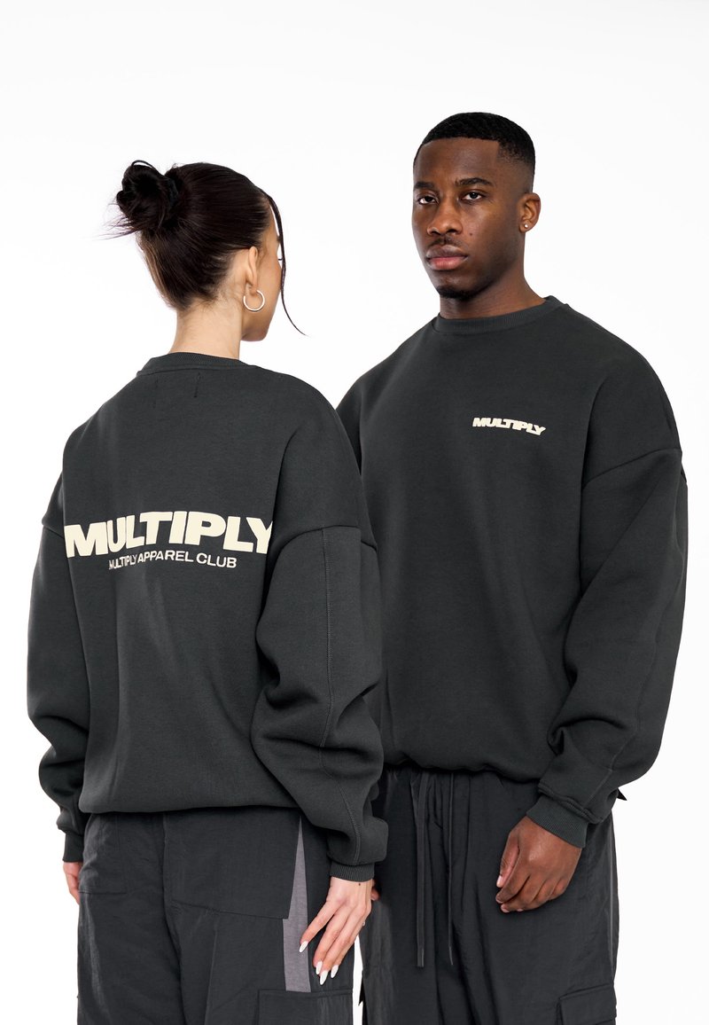 Tmavo šedé mikiny majú uvoľnený strih so spadnutými ramennými švami. Na chrbte je napísané "MULTIPLY" béžovými písmenami. Mäkká textúra, minimalistický štýl.